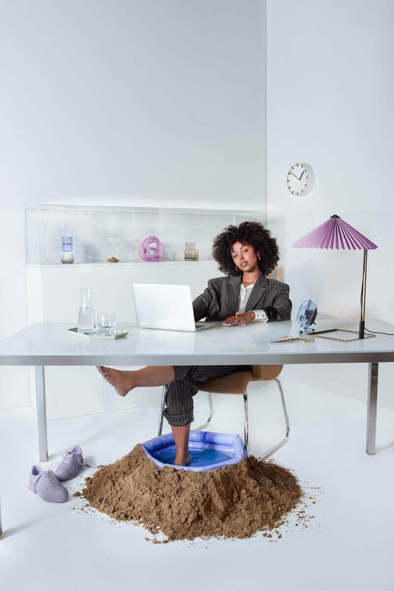 Vrouw aan haar bureau met de voeten in een badje met zand