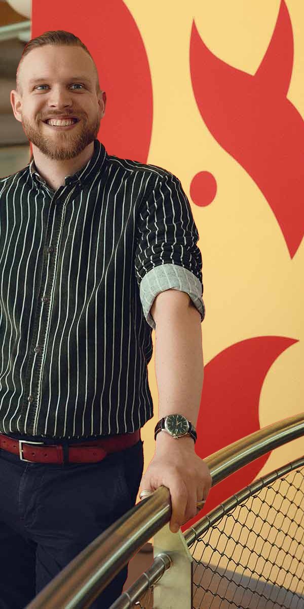 Mark leunt lachend op een trapleuning, voor een gele wand met rode eekhoorns