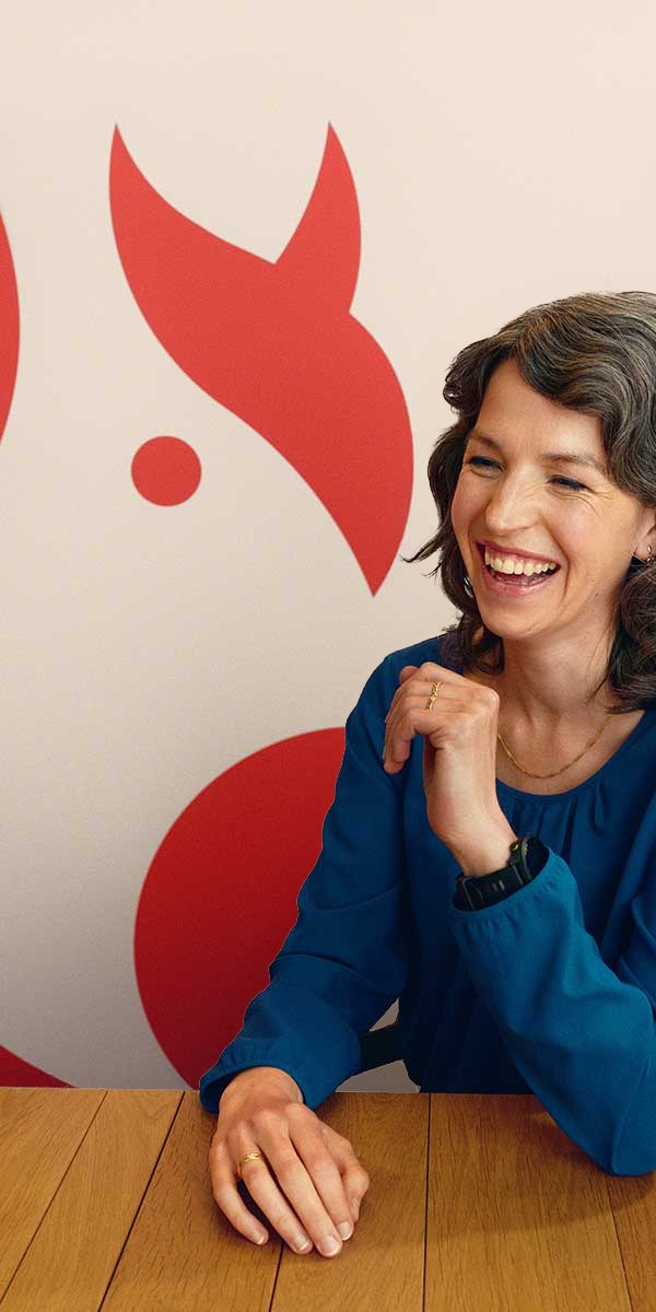 Yvonne lacht aan een houten tafel, voor de rode eekhoorn van ASN