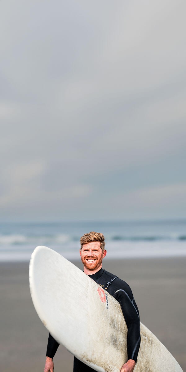 Maarten in wetsuit met een surfplank op het strand