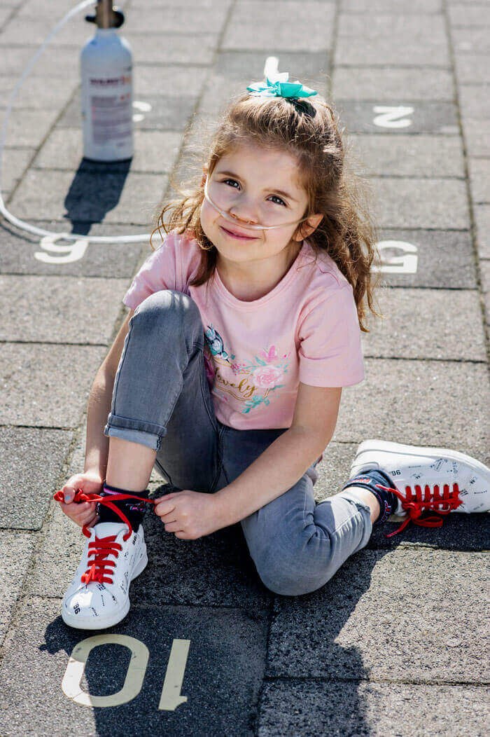Alyshia met zuurstofslangetje strikt haar rode veter op het schoolplein