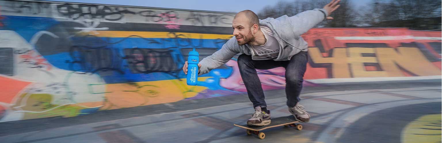 Een skateboarder met een waterfles voor een graffitimuur