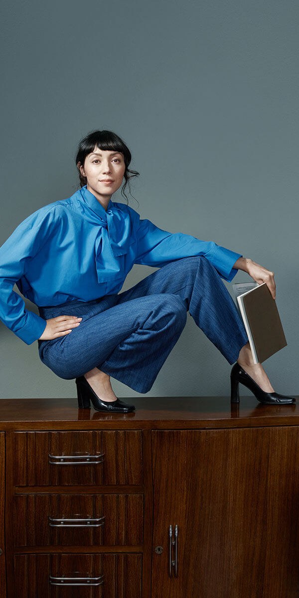 Juliet in een blauwe blouse, gehurkt op een kast