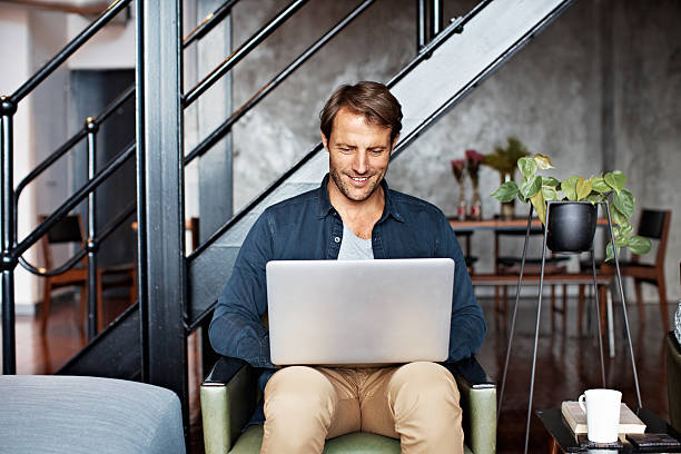 Shot of a mature man sitting on a chair in his living room using a laptop